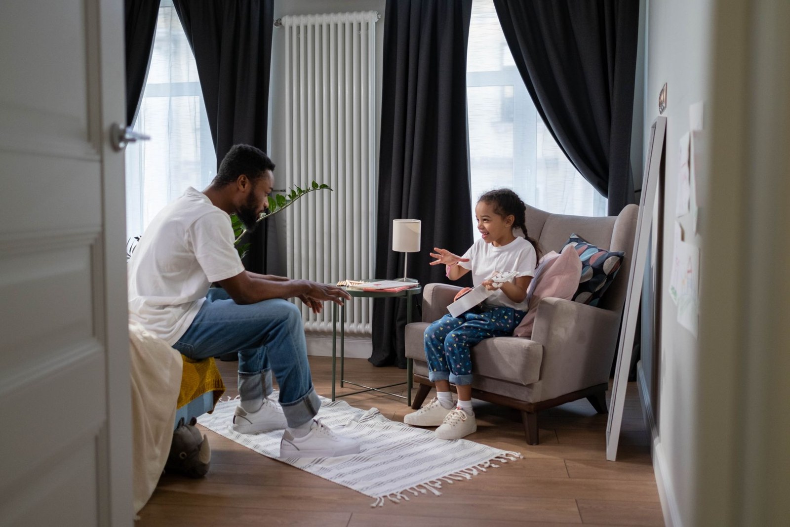 A father listens to his daughter, who is talking and holding a small guitar.